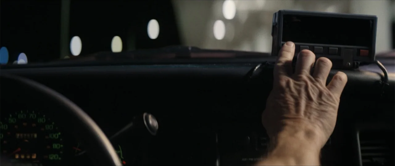 Daddio (2024) movie still: closeup — A dark vehicle interior shows a dashboard with an illuminated digital taximeter. A hand reaches in from the…