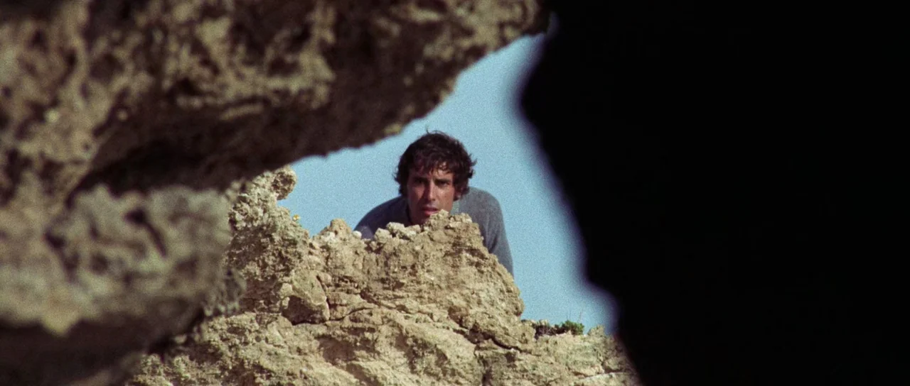 The Case of the Scorpion’s Tail (1971) movie still: medium — A man looks over a jagged limestone rock formation on a bright sunny day. The…