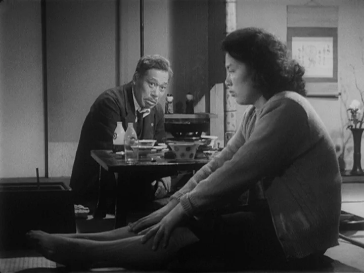 Ikiru (1952) movie still: medium — A traditional Japanese room features a low wooden table and tatami mat flooring. An older man in a suit looks at…