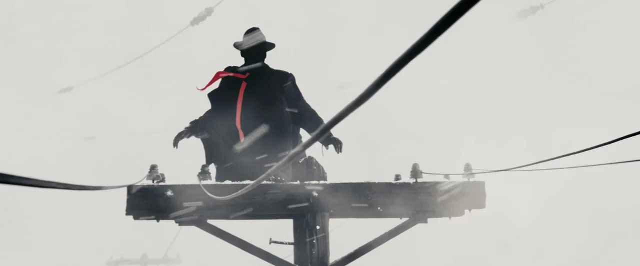 The Spirit (2008) movie still: medium — A wooden utility pole stands in a bright white, snow-filled expanse. A silhouetted figure in a fedora sits…