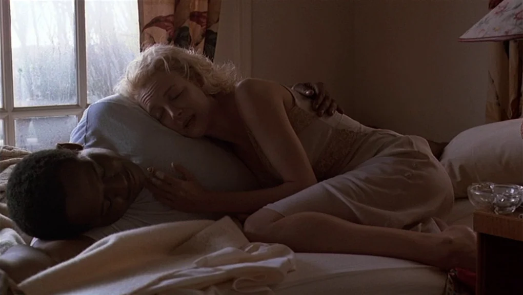 Bird (1988) movie still: medium — A dimly lit room with a window showing a daytime exterior. A woman rests her head on the shoulder of a man in bed.