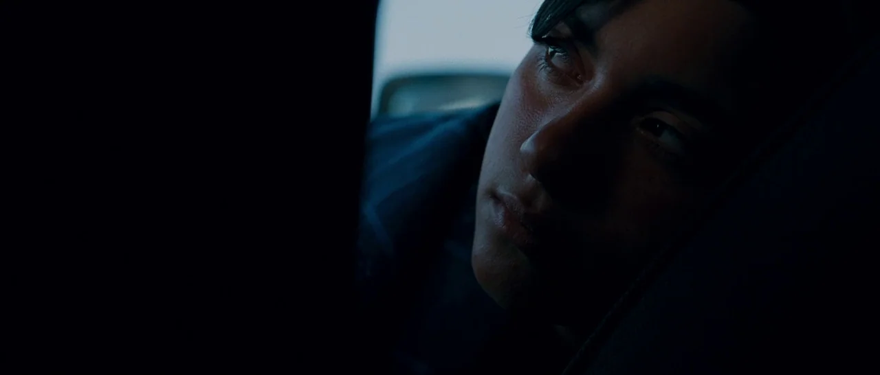 Sin Nombre (2009) movie still: closeup — The interior of a dark car at night shows a person leaning back. The occupant gazes toward the window while…