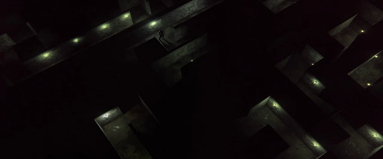 Revealer (2022) movie still: establishing — A complex maze structure features high concrete walls arranged in long geometric pathways. A single…