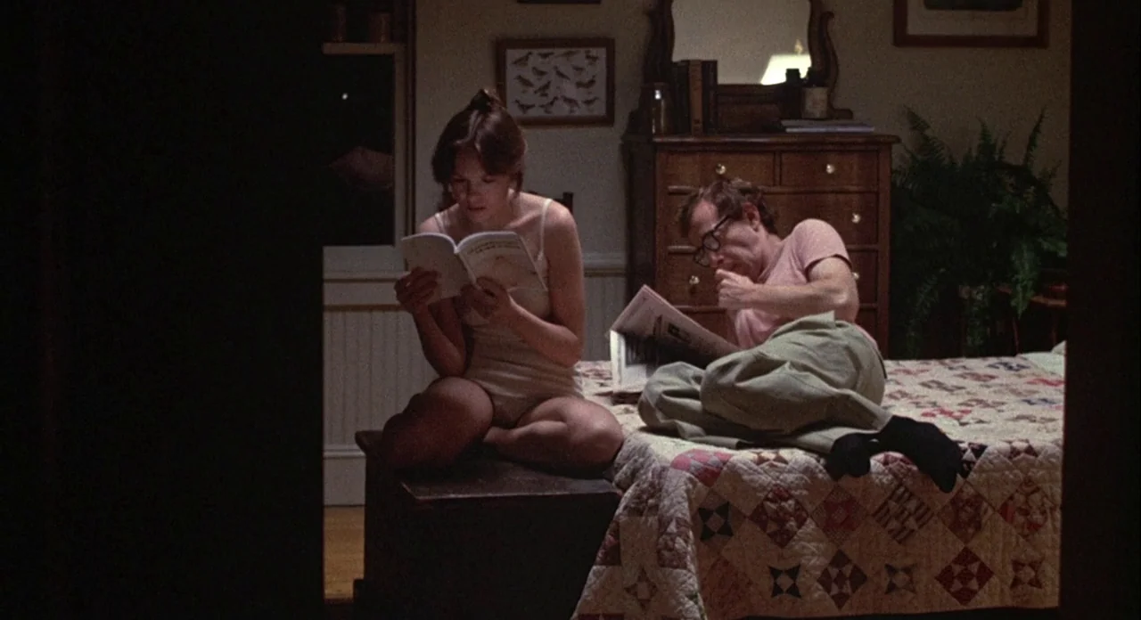 Annie Hall (1977) movie still: medium — A dimly lit bedroom features a wooden dresser and a quilt-covered bed at night. A young woman sitting on a…