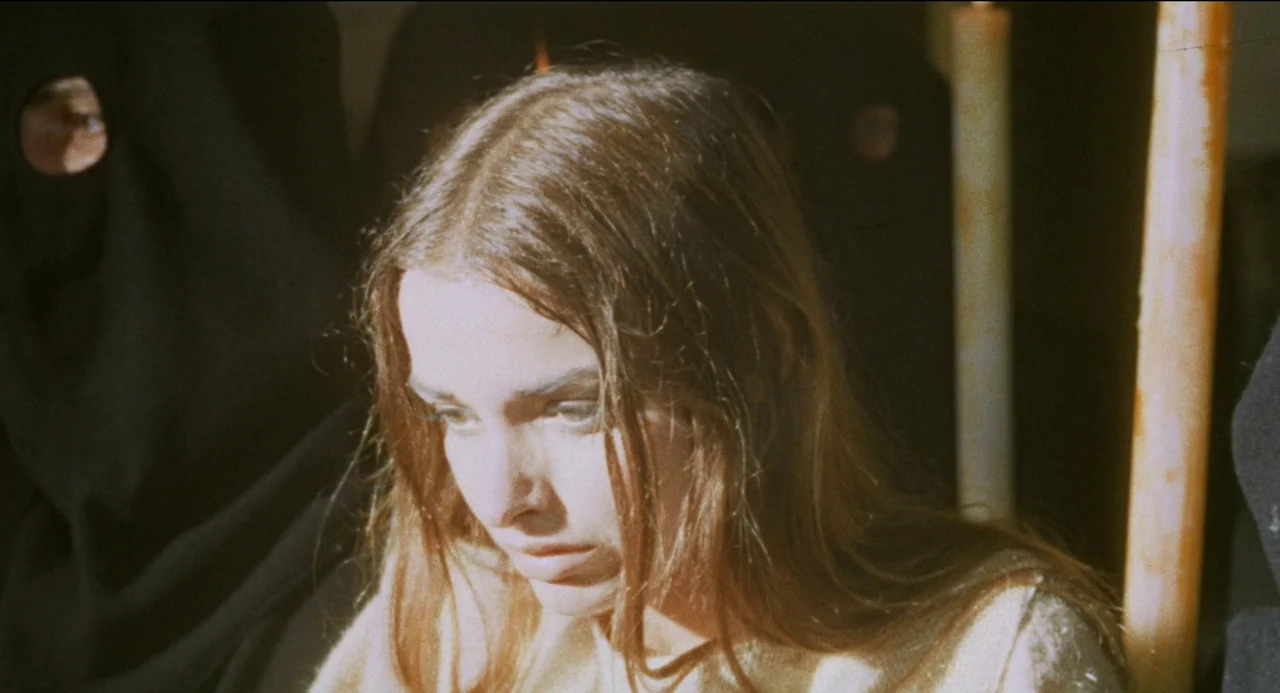 Beatrice Cenci (1969) movie still: closeup — A dimly lit interior space with a person partially visible in a black hood. A woman with long hair…