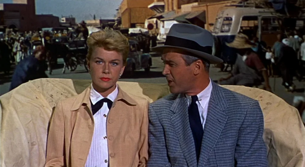 The Man Who Knew Too Much (1956) movie still: medium — A bustling North African market street features pedestrians and vintage vehicles in the…
