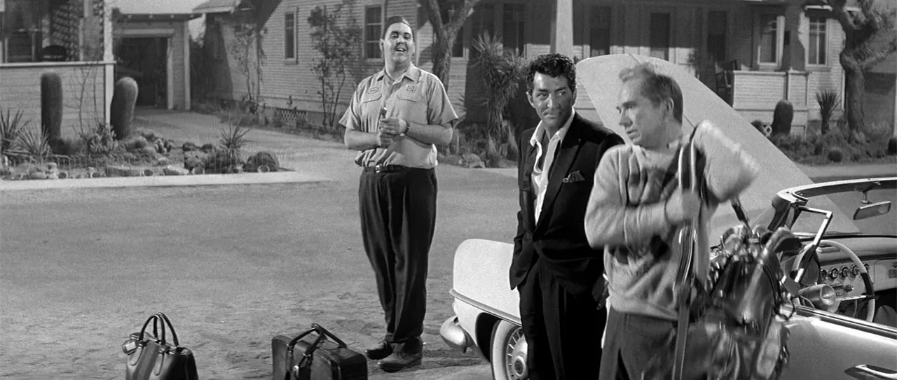 Kiss Me, Stupid (1964) movie still: fullbody — A suburban house exterior with a gravel driveway and a parked convertible car. Three men stand near…
