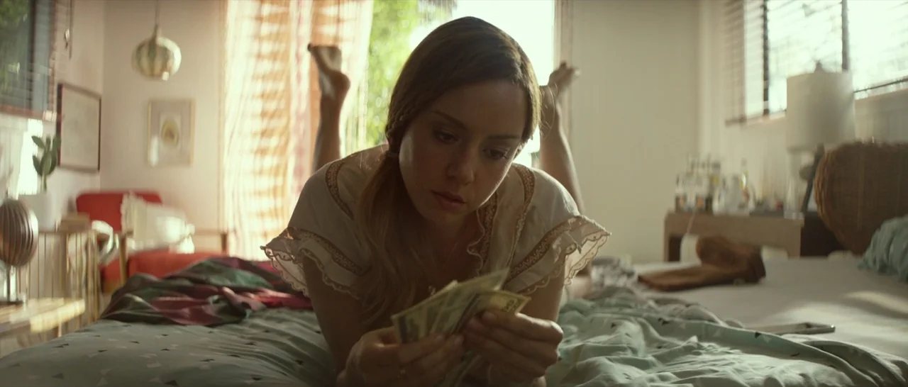 Ingrid Goes West (2017) movie still: medium — A light-filled room features a person reclining on a patterned bedspread near a window. The subject…