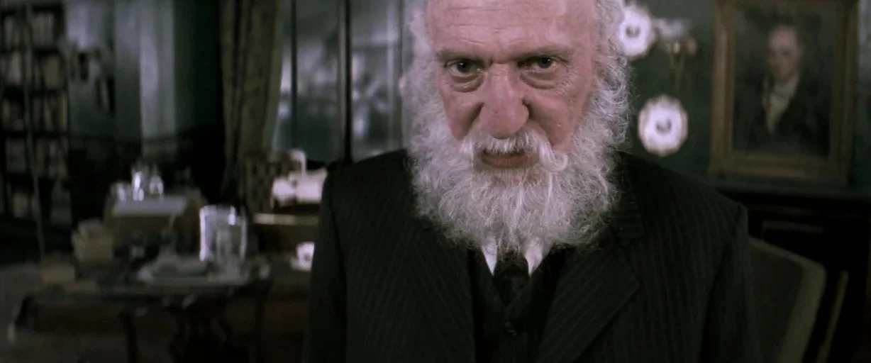 Moulin Rouge! (2001) movie still: closeup — A dimly lit room contains wooden furniture and framed portraits on the wall. The elderly man stands in…