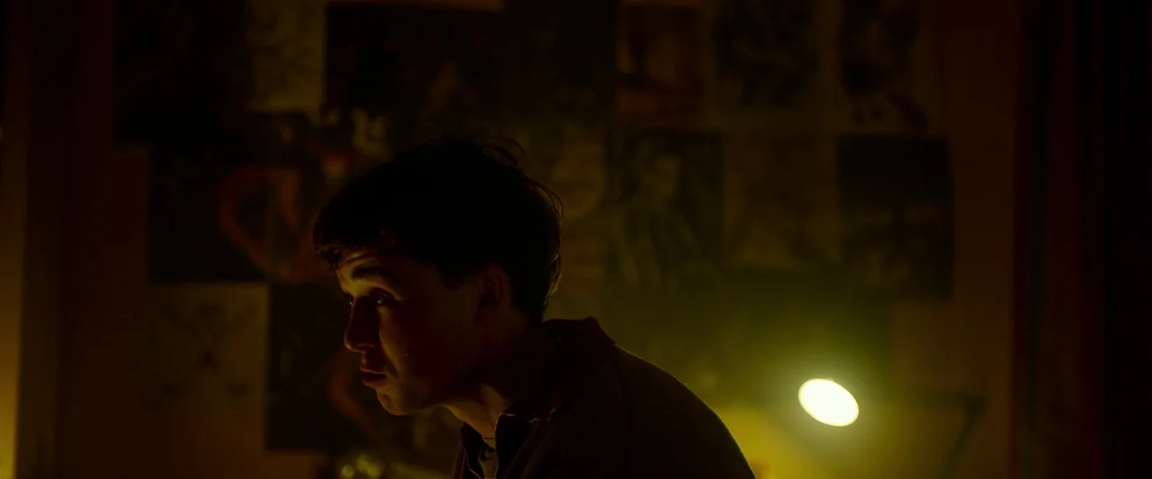 Ghost Stories (2017) movie still: medium — A dark bedroom interior features walls covered with various framed art prints and photographs. A young…