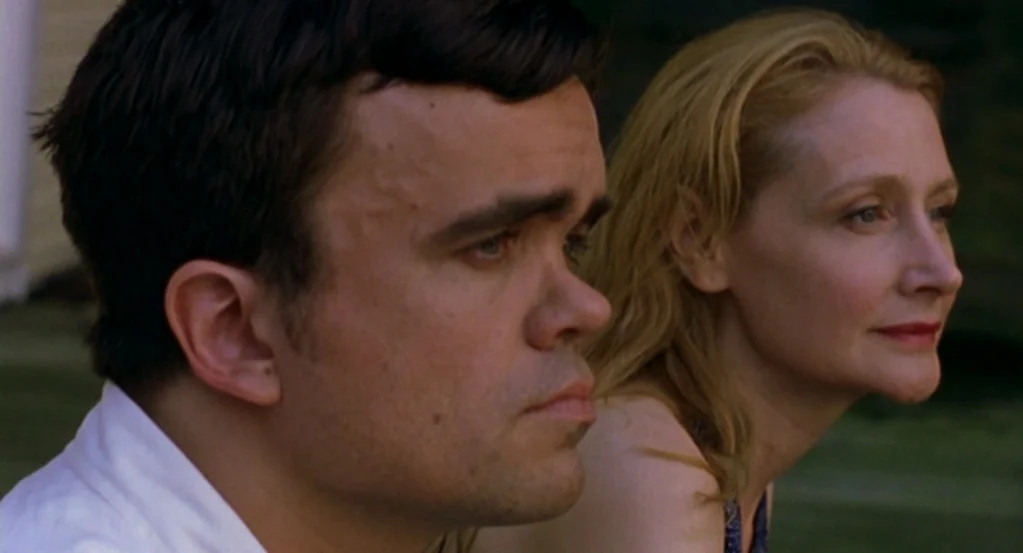 The Station Agent (2003) movie still: medium — Two individuals sit together in an outdoor space bathed in soft natural daylight. They gaze forward,…
