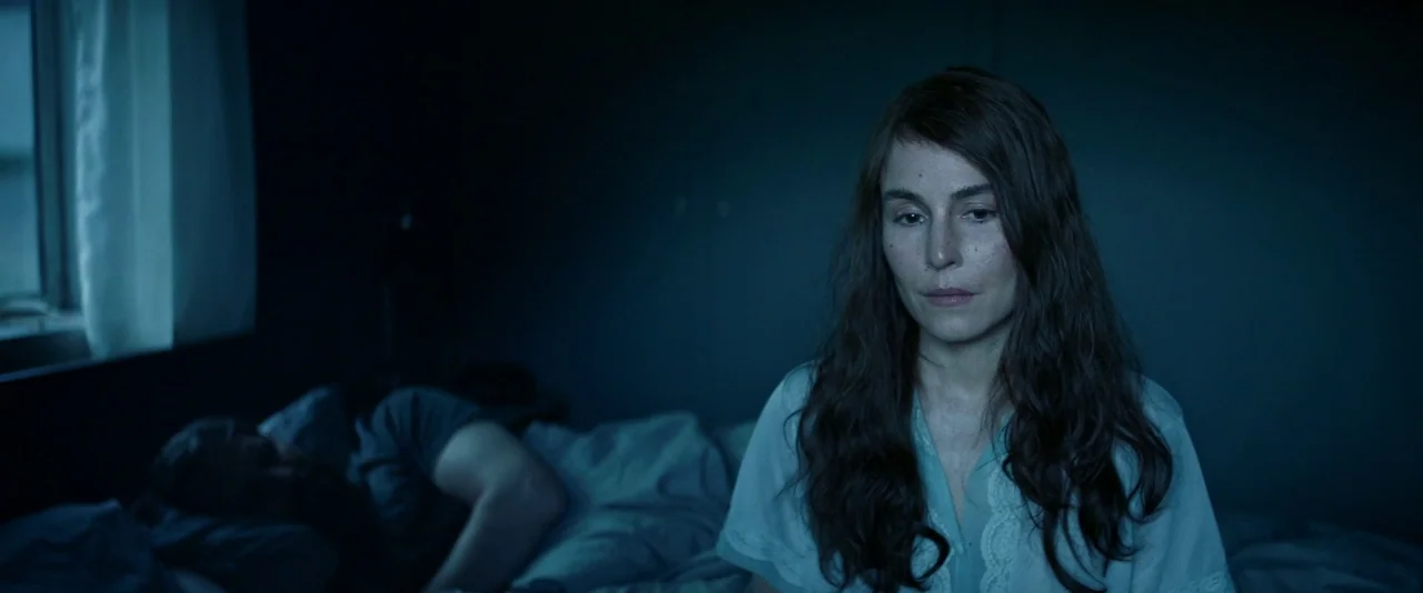 Babel (2006) movie still: medium — A dimly lit room at night with deep blue shadows and cool tones throughout. A woman sits on the edge of a bed as…