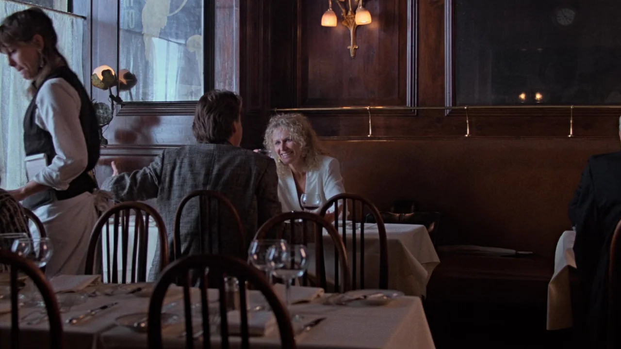 Fatal Attraction (1987) movie still: medium — A dark, wood-paneled dining space features white-clothed tables and dim wall lighting. A man and woman…