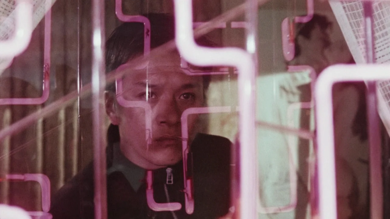 Suzhou River (2000) movie still: closeup — A man peers through a transparent display containing glowing pink neon tubing. The background is dimly…