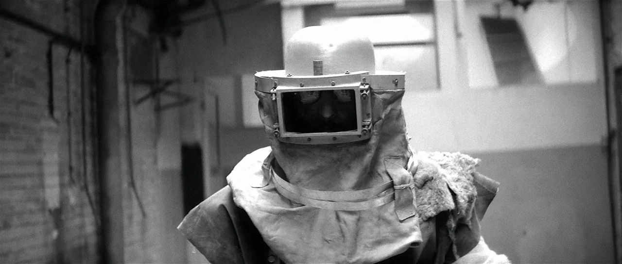 The Last Battle (1983) movie still: medium — An industrial workspace with brick walls and blurred structural elements in the background. A person…