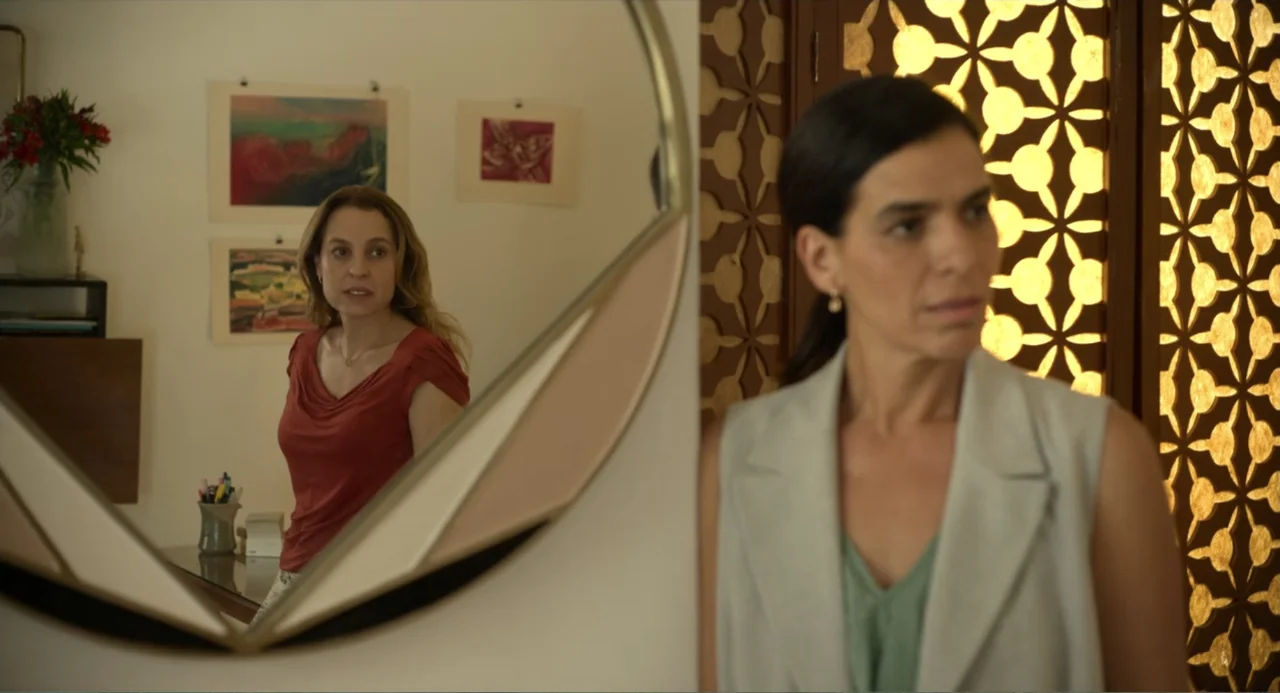 Heartbeat (2008) movie still: medium — A well-lit interior room features a circular mirror reflecting a second woman standing behind. One woman…