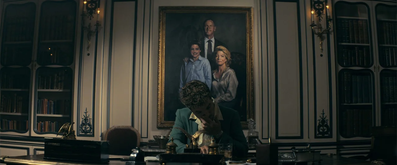 The Beekeeper (2024) movie still: medium — A wood-paneled study features a large family oil painting mounted above a desk. A man sits at the desk,…