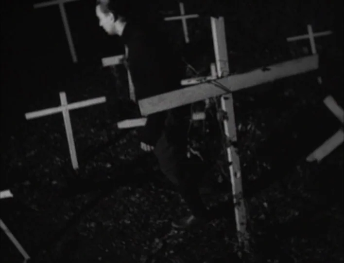 Tales from the Gimli Hospital (1988) movie still: fullbody — A dark, high-contrast cemetery scene filled with numerous small white wooden crosses. A…