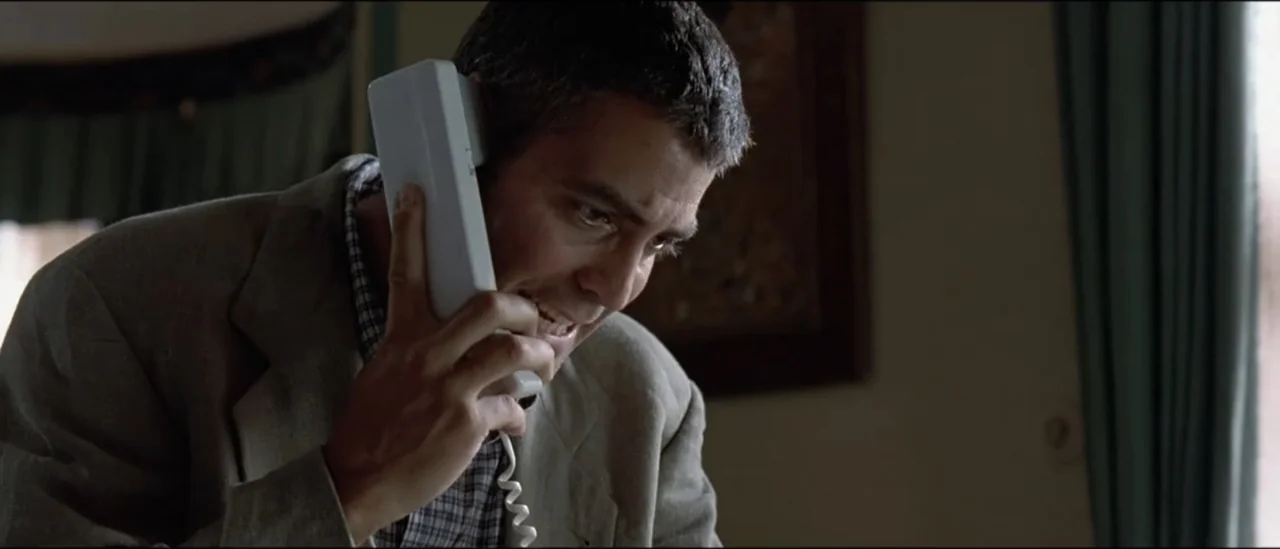 The Peacemaker (1997) movie still: medium — A domestic hotel room interior with blurred green curtains visible in the background. A man in a beige…