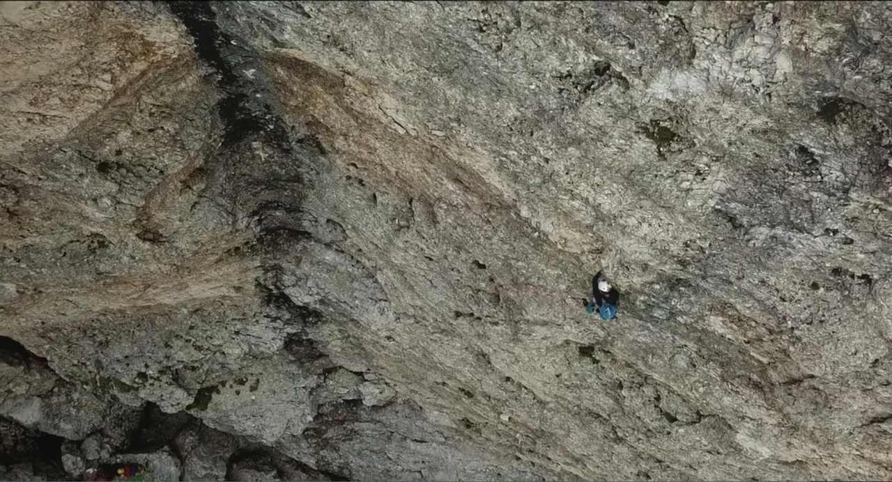 Crooked Trees Gon Give Me Wings (2022) movie still: wide — A vast and rugged limestone cliff face fills the entire frame. A lone climber maneuvers…