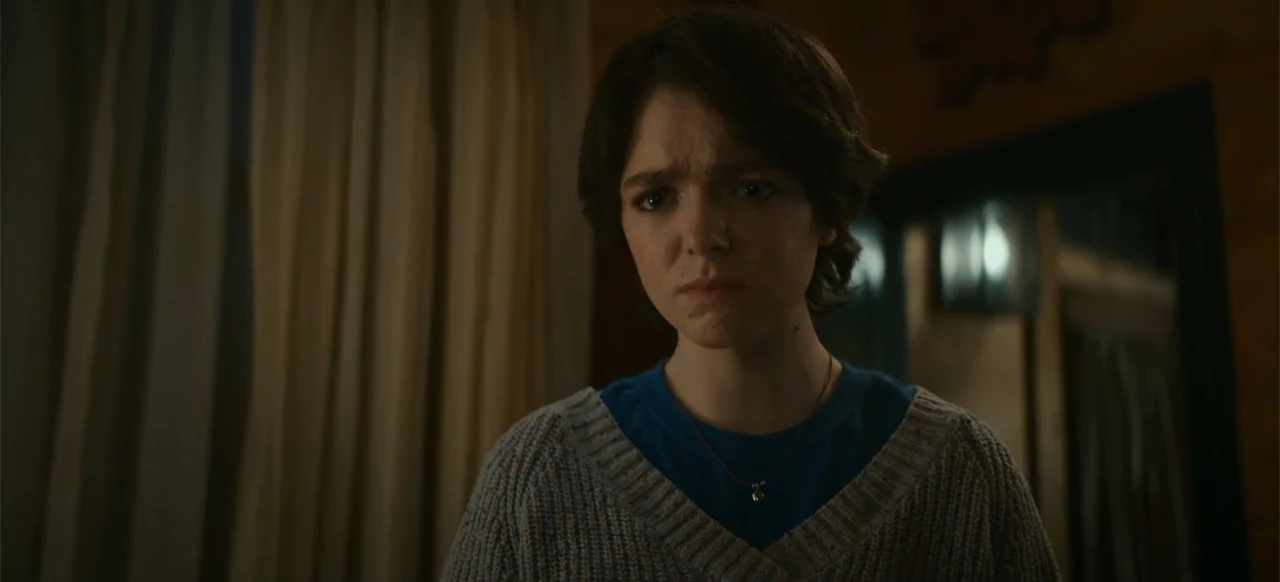 My Best Friend's Exorcism (2022) movie still: medium — A dark indoor space with beige curtains and wood paneling in the background. A young woman…
