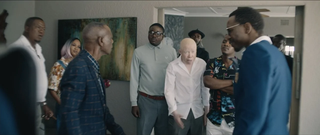 My Girlfriend's Father (2023) movie still: medium — A group of diverse men and women stand inside a modern home interior. The individuals are…