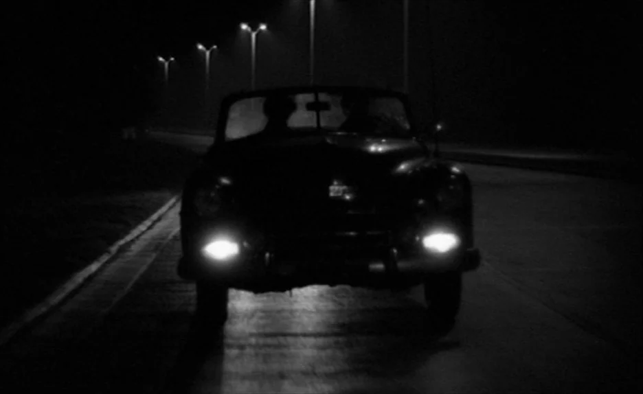Elevator To The Gallows (Ascenseur pour l’échafaud) (1958) movie still: medium — A vintage convertible drives toward the camera along a dark, empty…