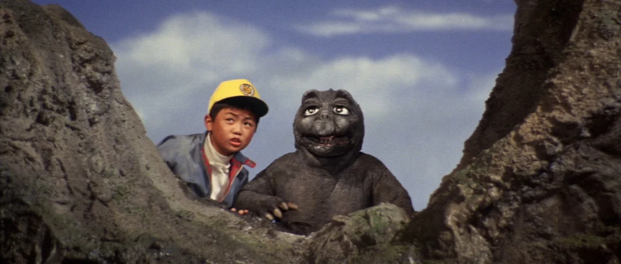 All Monsters Attack (1969) movie still: medium — A craggy, rocky landscape with a blue sky visible in the upper background. A young boy and a small…