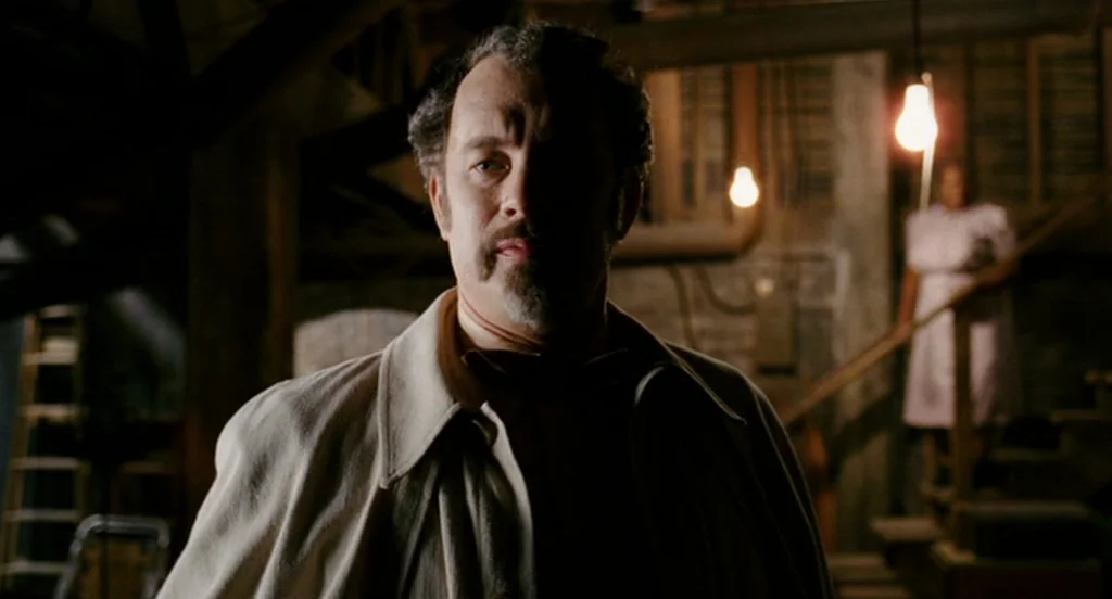 The Ladykillers (2004) movie still: medium — An attic with exposed wooden rafters and dim light bulbs hanging from the ceiling. A man in a trench…