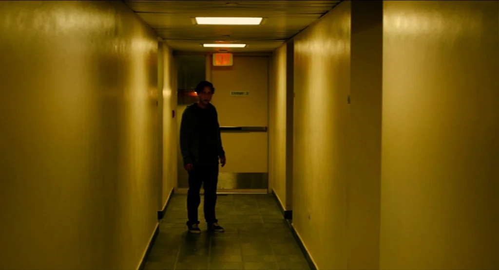 Life During Wartime (2009) movie still: fullbody — A long, dimly lit indoor corridor has yellow walls and a tiled floor. A single person stands by…