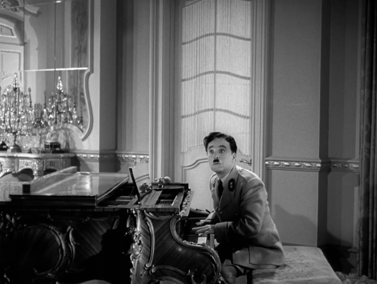 The Great Dictator (1940) movie still: medium — A formal drawing room features a polished wooden piano and an ornate wall mirror. A man in a…