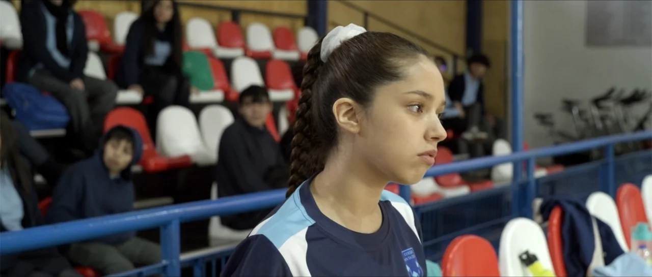 Disconnected 2 (2025) movie still: medium — An indoor bleacher section features rows of white and red plastic stadium seats. A young female athlete…
