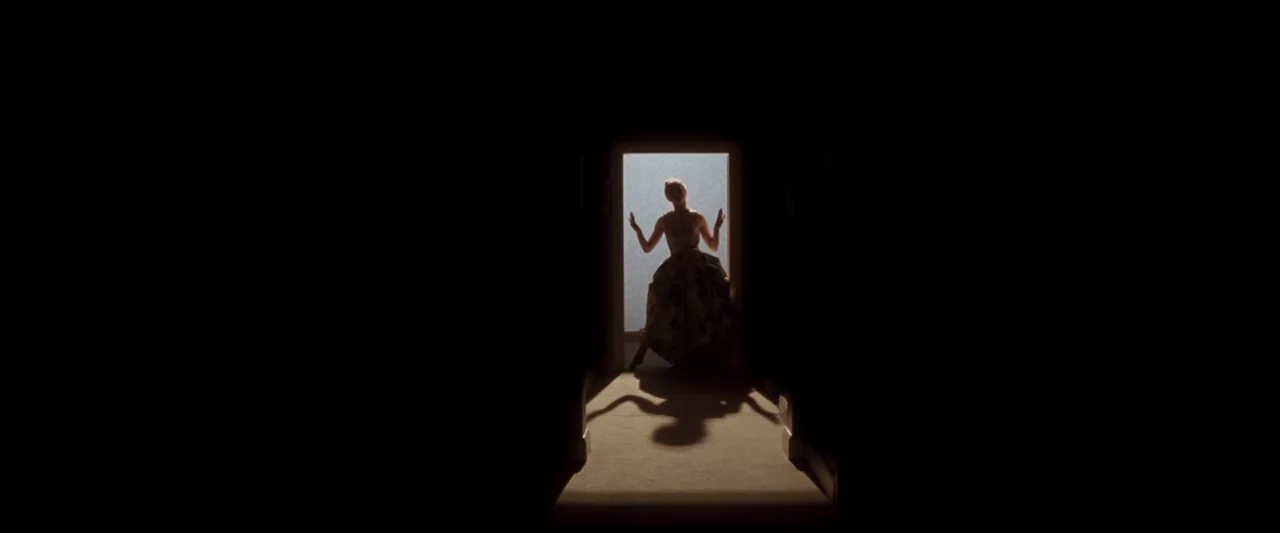 Last Night in Soho (2021) movie still: wide — A silhouette of a woman appears inside a brightly lit rectangular doorway frame. The surrounding…