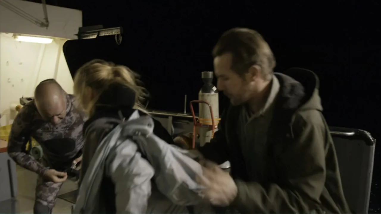 Megalodon: The Monster Shark Lives (2013) movie still: medium — A dark, cramped boat deck with metallic surfaces and equipment at night. Two men and…