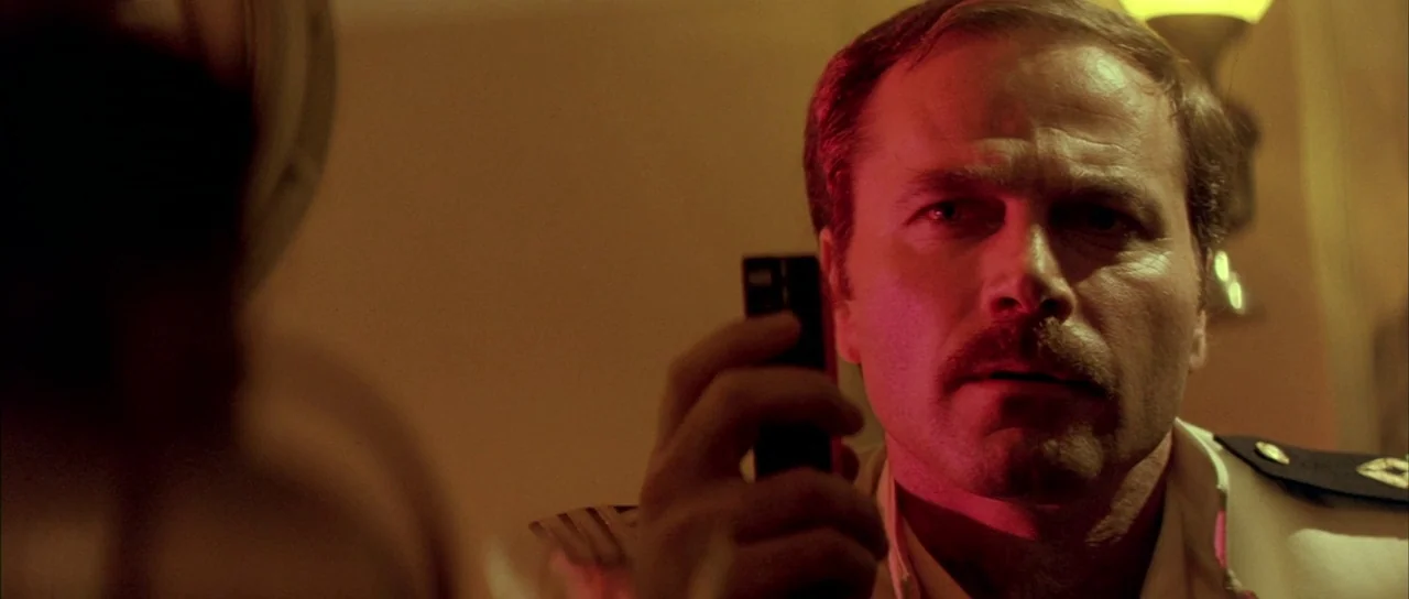 Querelle (1982) movie still: closeup — A dimly lit room with industrial piping and metallic walls visible. A man in a naval uniform stares intensely…