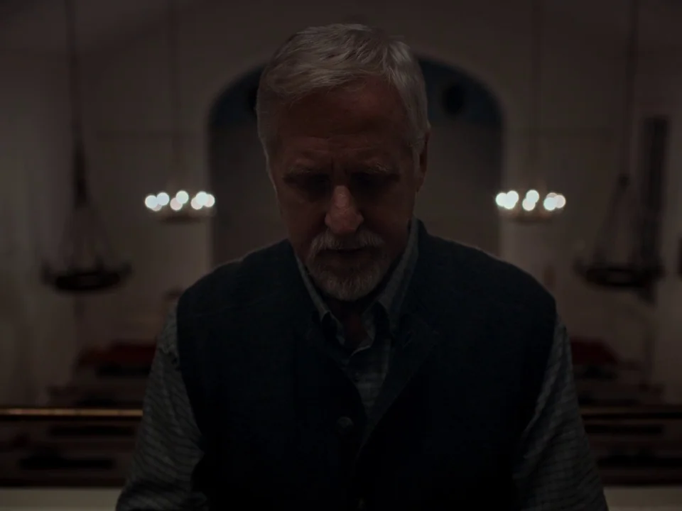 First Reformed (2017) movie still: medium — A dimly lit church sanctuary features blurry, glowing chandeliers against a dark, featureless backdrop.…