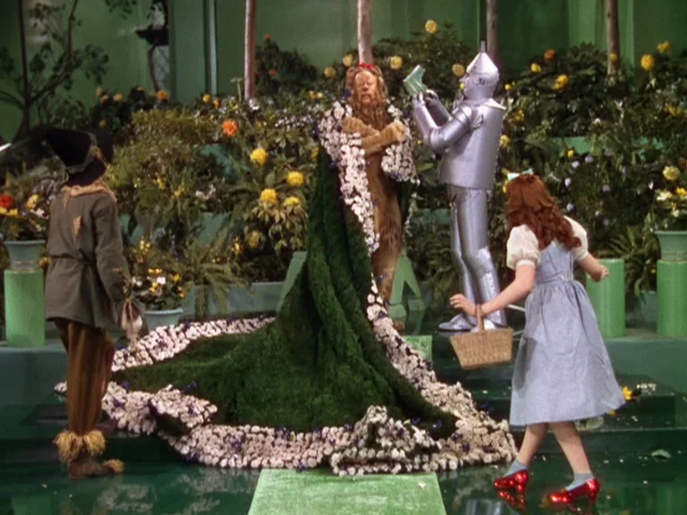 The Wizard Of Oz (1939) movie still: fullbody — An opulent palace interior features green flooring and numerous blooming potted floral arrangements.…