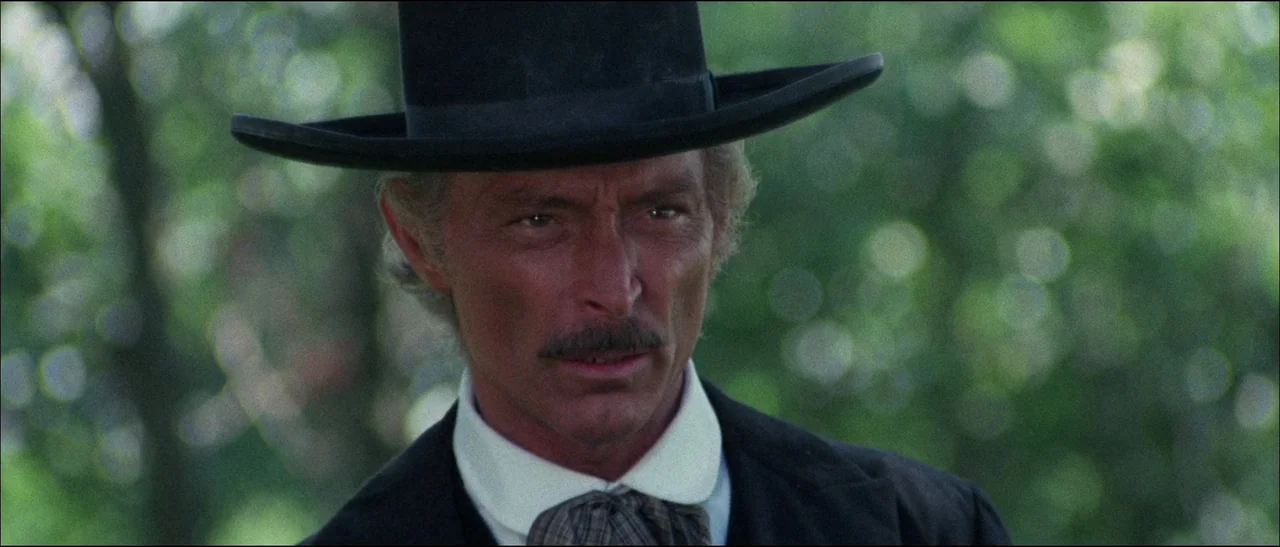 The Grand Duel (1972) movie still: closeup — A man in nineteenth-century attire stands outdoors in front of a dense green forest. He stares forward…