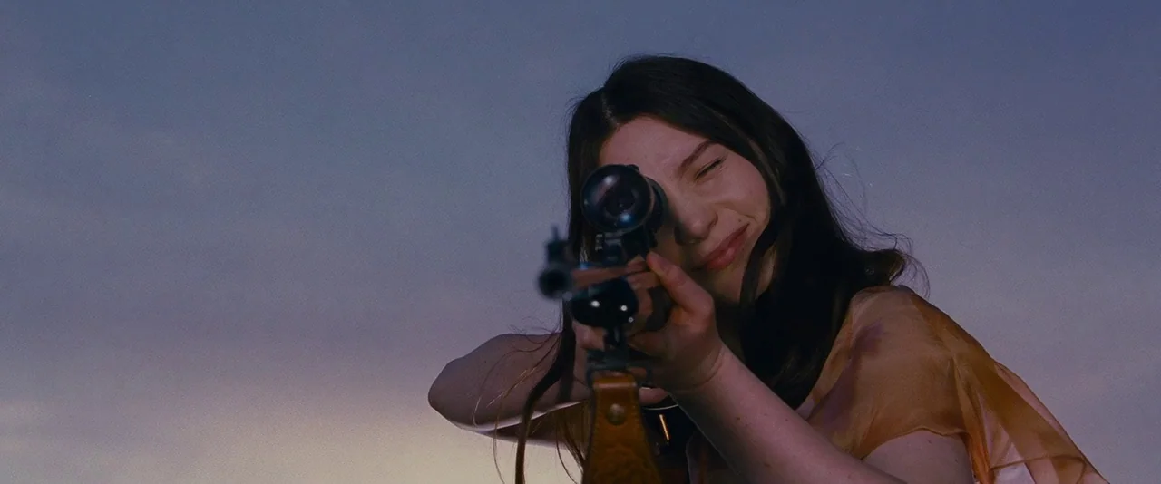 Stoker (2013) movie still: closeup — A woman stands outdoors during twilight, looking through the scope of a hunting rifle. She holds the weapon…