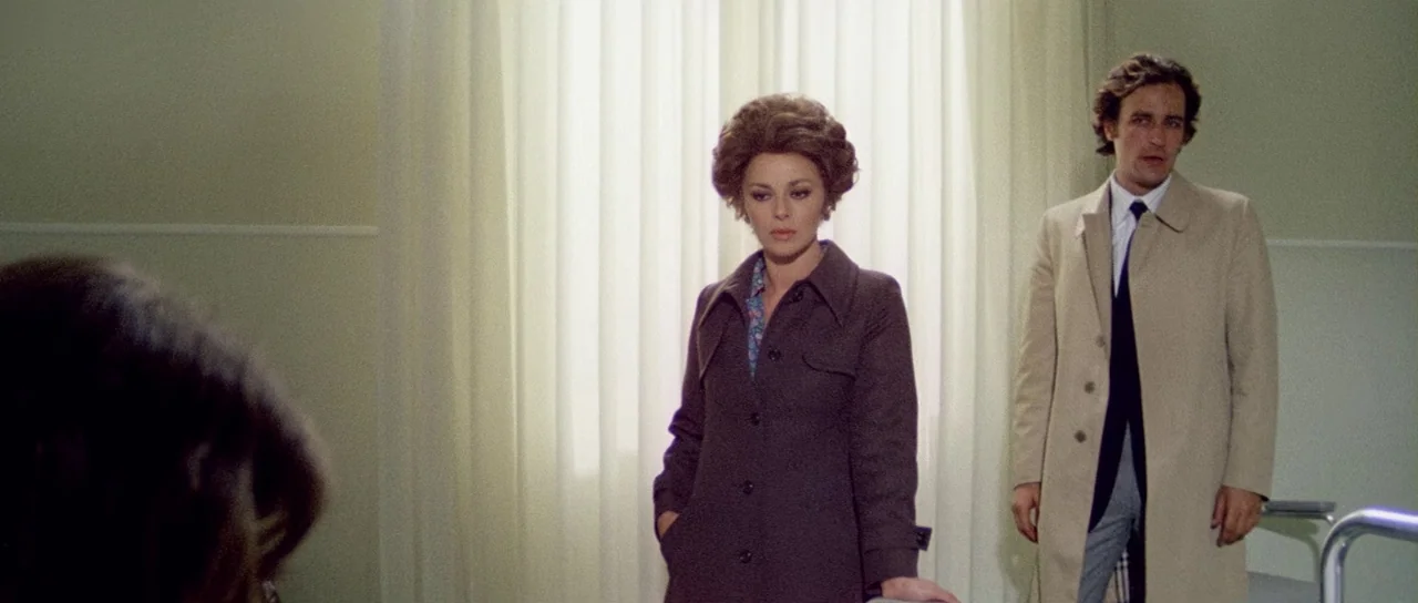 What Have They Done To Your Daughters? (1974) movie still: medium — A room with pale green walls and large sheer curtains covering a window. A woman…