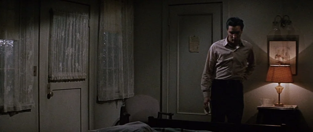 Wild in the Country (1961) movie still: medium — A dimly lit room with lace-covered windows and a simple bedside lamp. A man stands beside a lamp,…