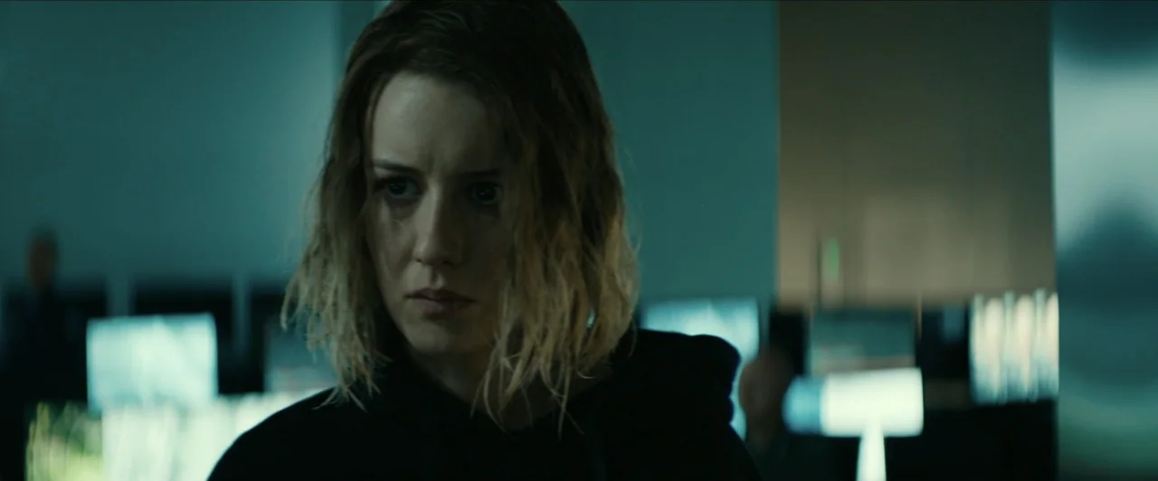 Invasion (2020) movie still: closeup — A dark tech workspace contains multiple glowing computer screens. A woman with damp hair gazes toward the…