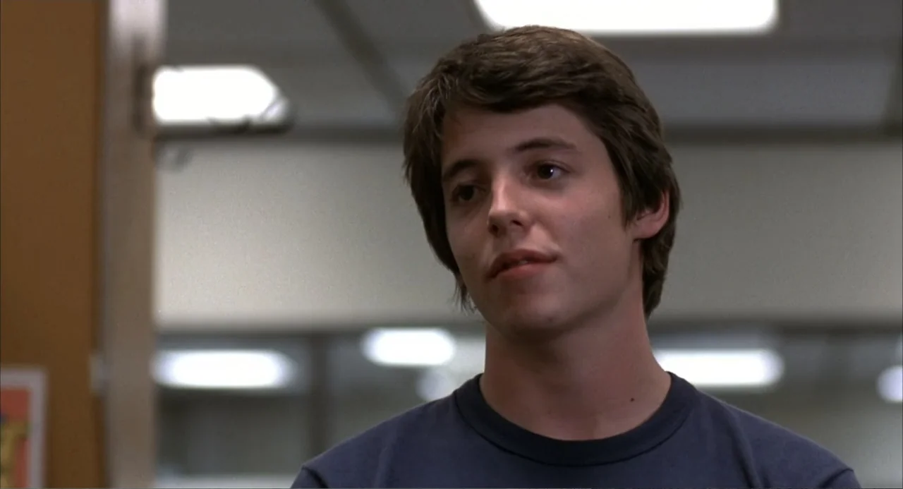 WarGames (1983) movie still: medium — A 1980s school hallway features cream-colored walls and overhead fluorescent lighting fixtures. A young man…