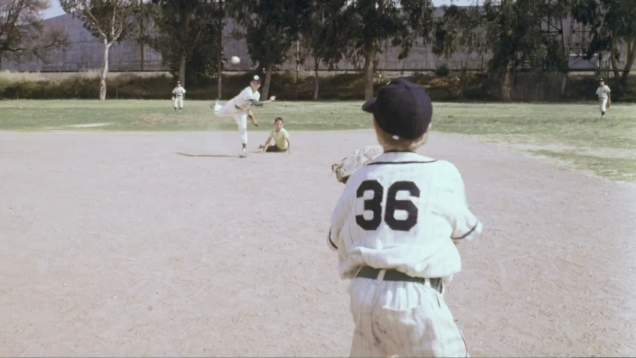 Aunt Mary (1979) movie still: medium — A dusty dirt baseball diamond with young boys in vintage uniforms playing a game. A child stands in the…