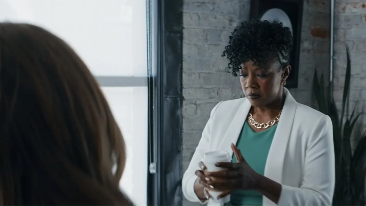 Making Waves (1998) movie still: medium — An office space with exposed brick walls and a large window. A woman in a white blazer holds a takeaway…