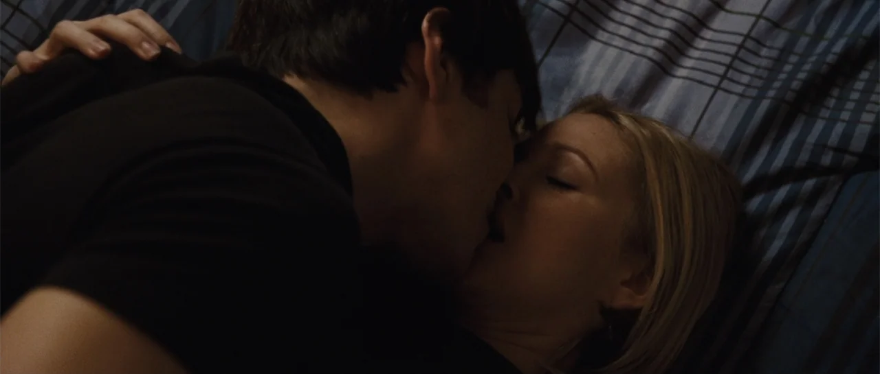 Going the Distance (2010) movie still: closeup — A dark room features a blue and brown plaid bedspread as the backdrop. A man and a woman lie…