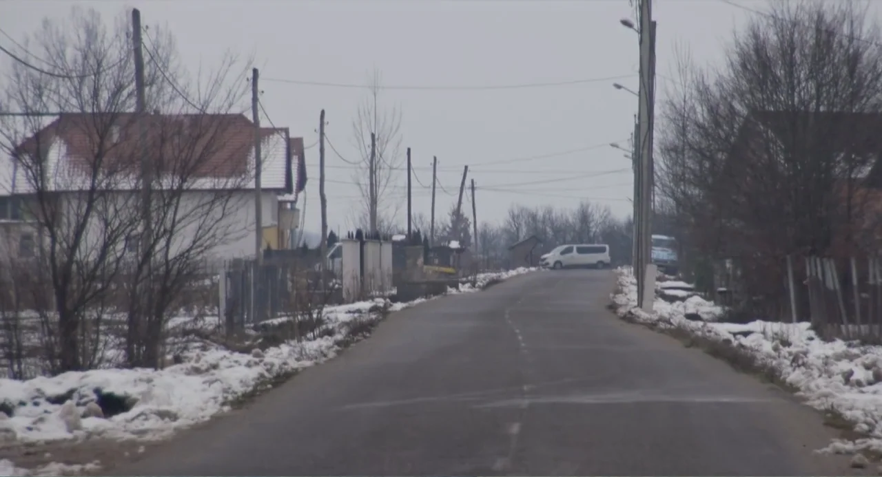 A Dramatic Film (2019) movie still: establishing — A paved road stretches into the distance, bordered by patchy snow and leafless trees. A white van…