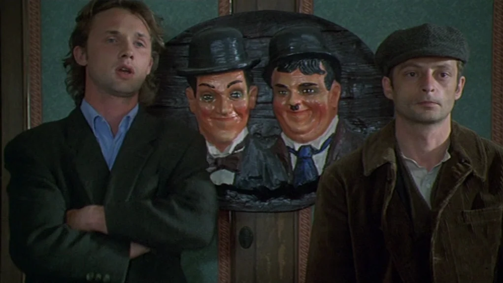 One Hundred and One Nights (1995) movie still: medium — A green-walled interior features a centered dark wood plaque with faces of Laurel and Hardy.…