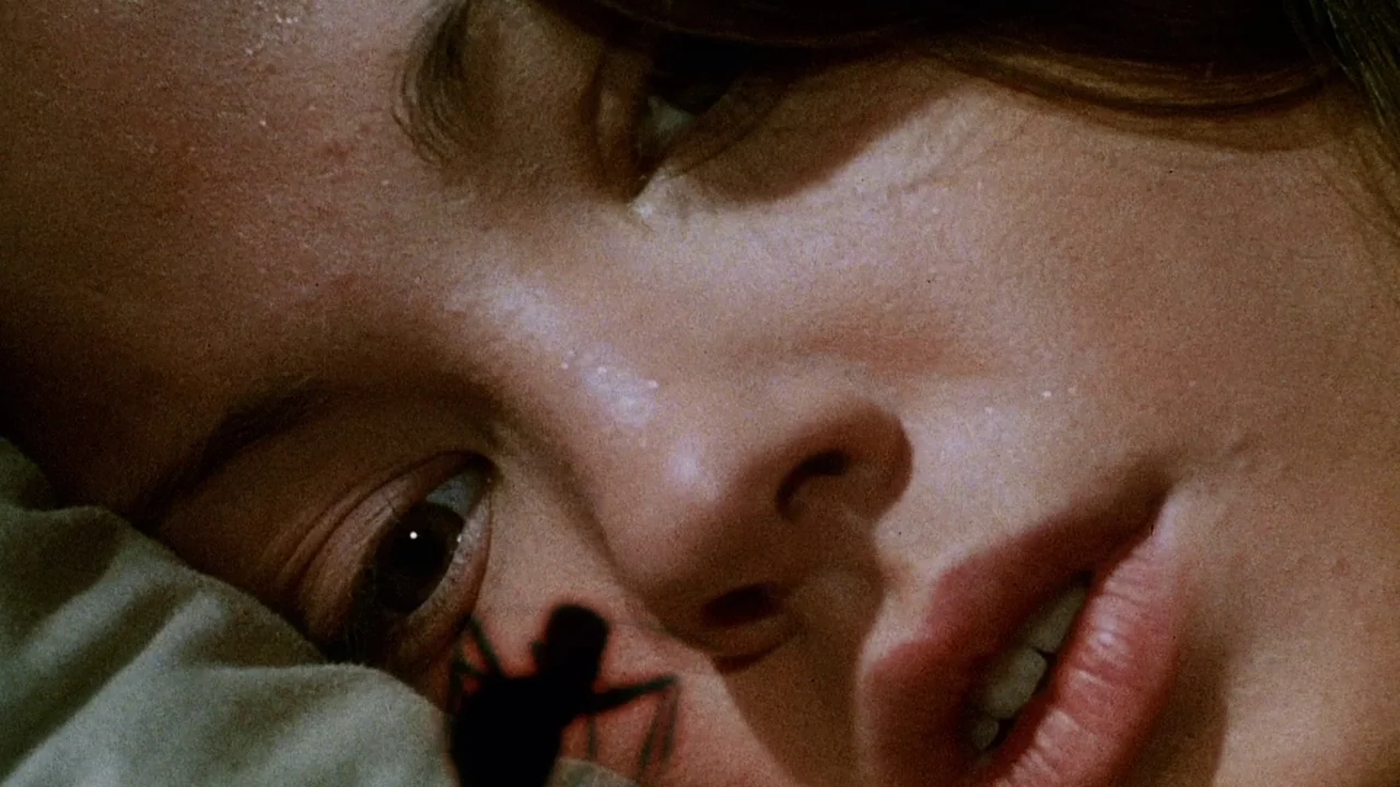 Phase IV (1974) movie still: closeup — A close-up captures a woman lying on a pillow in a dimly lit room. A small black ant crawls across her cheek…