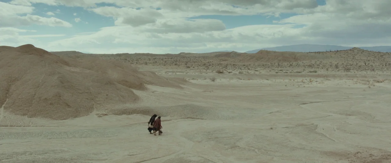 Last Days in the Desert (2015) movie still: wide — An arid, sprawling desert basin with textured dunes and distant rolling hills under clouds. Two…